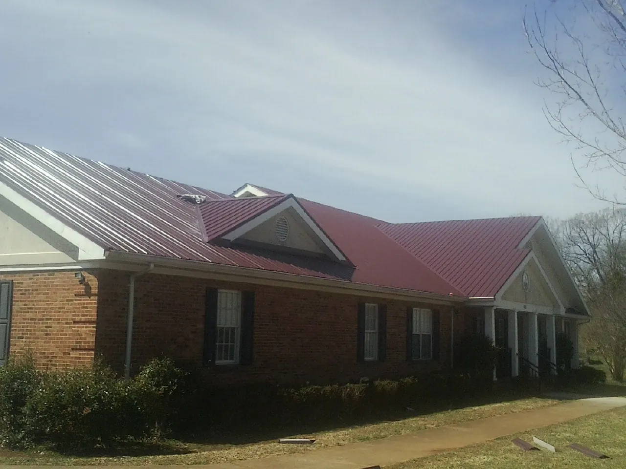 Red metal roof with gabled entries on a long brick building, from a Hail Damage Roof Repair job in Paden City