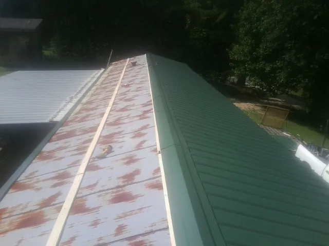 Old rusted panels beside newly installed green metal roofing — Wind Damage Roof Repair by Roofing Brothers in Paden City
