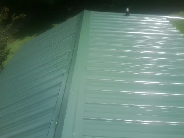 New green metal panels meeting at the ridge of a roof — Flat Roof Repair work by our crew in Paden City
