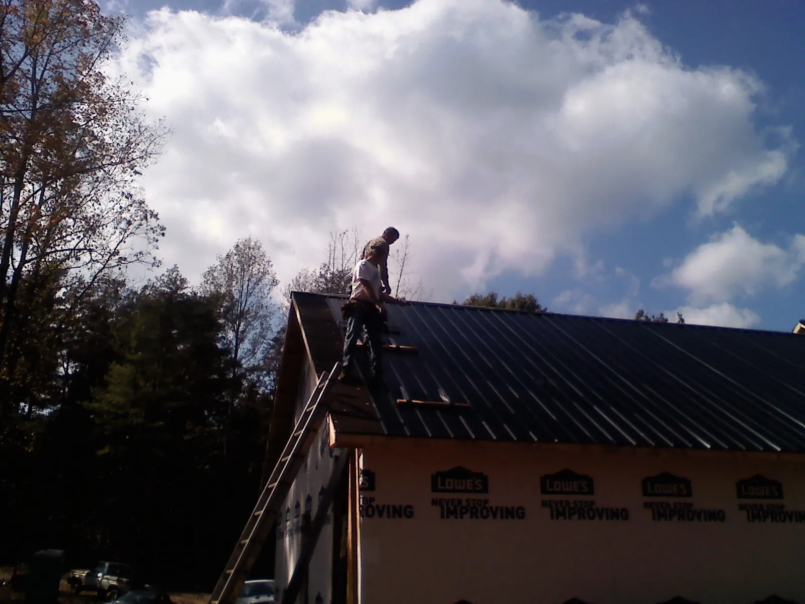 Roofer fastening dark metal panels high against a cloudy sky, from a Roof Inspection job in Paden City