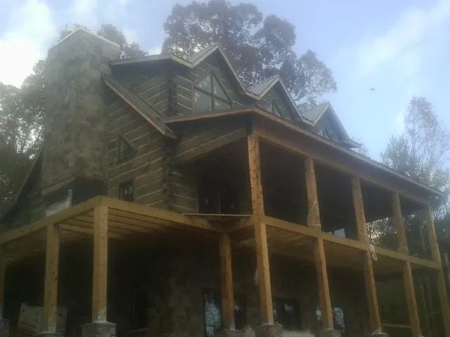 Stone chimney and dormers on a large log home with a timber porch in Paden City