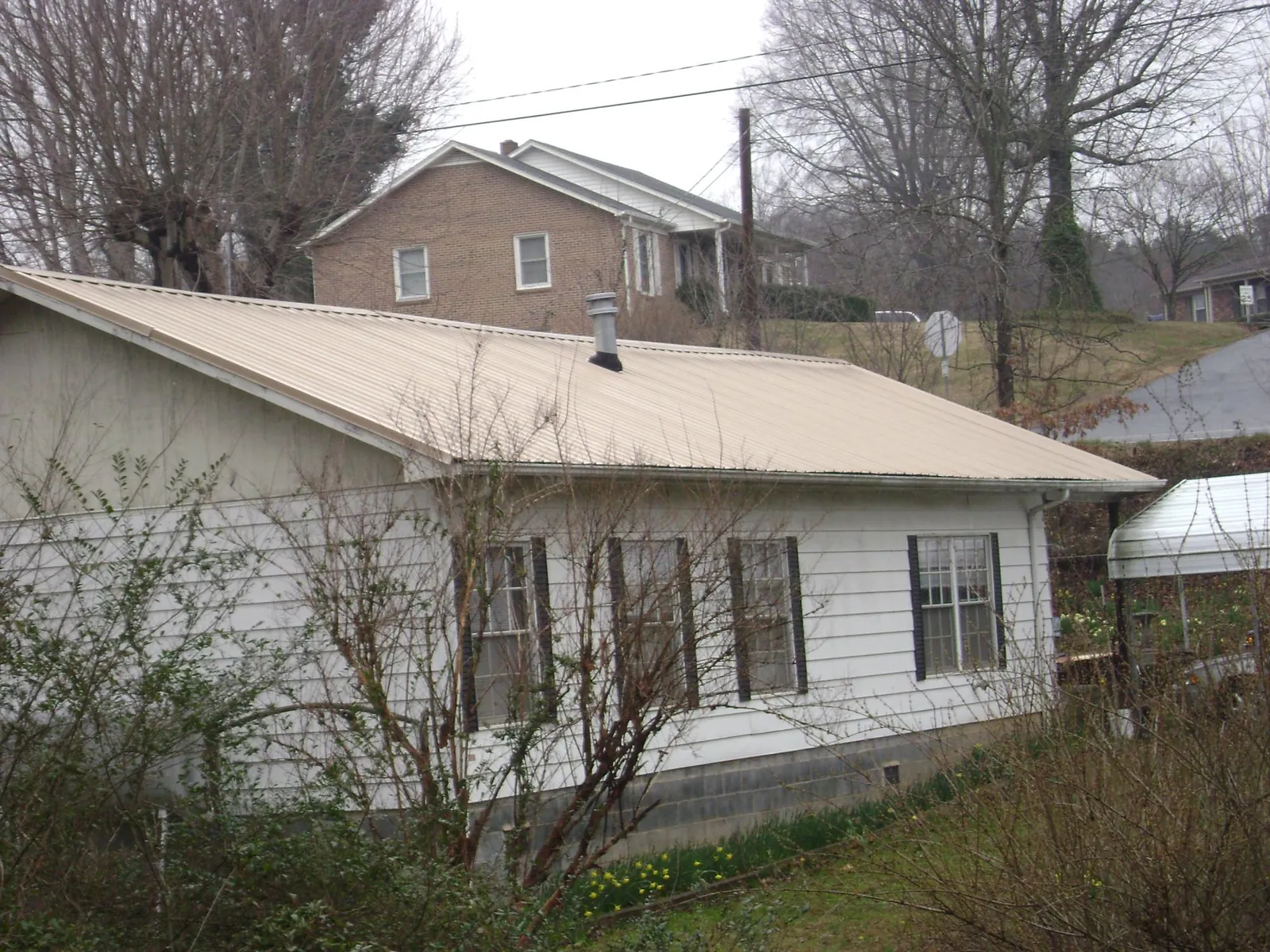 Tan metal roof on a white sided house set into a hillside — Commercial Roofing by Roofing Brothers in Paden City